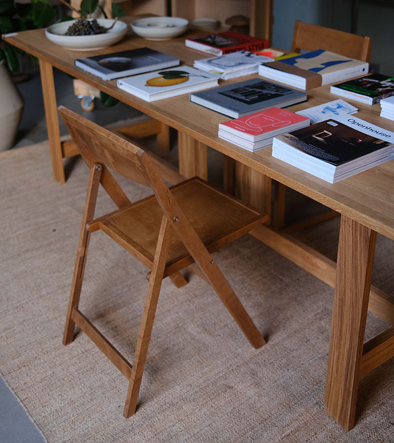 Frama Folding Flat Chair designet av Casegoods ved Kollekted by en interiørforretning på Grunerløkka i Oslo. Klapptolen er i Warm Brown. Bidet viser Farmhouse Table og bøker fra blant annet Apartamento 